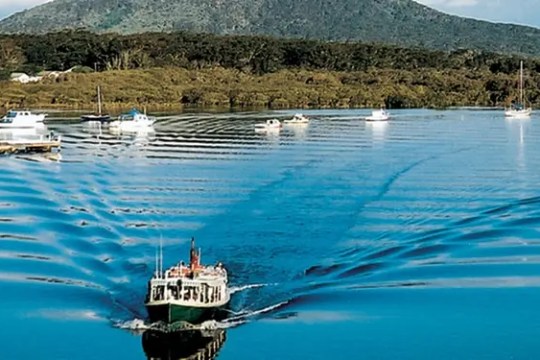 Boat sailing on calm water with lush green hills in the background.