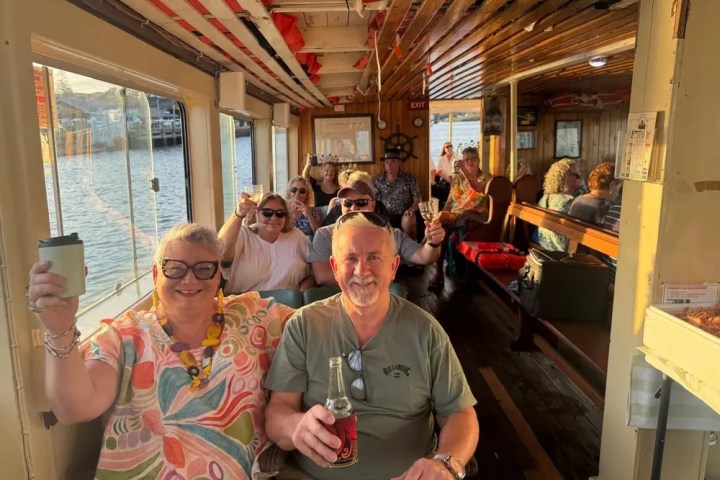 Group of people smiling and holding drinks on a boat with wooden interior.