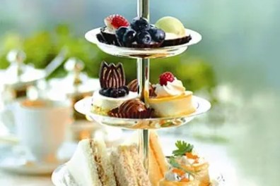 Three-tier tray with sandwiches, pastries, and fruit.