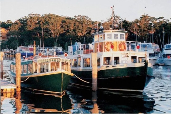 Two vintage boats moored at a wooden dock with trees in the background.