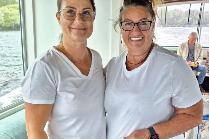 Two women smiling on a boat, both wearing white t-shirts.