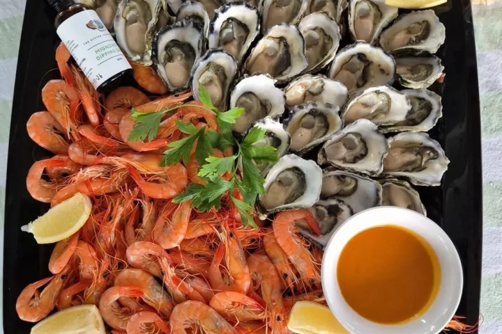 Plate of oysters and prawns with lemon wedges and sauce.