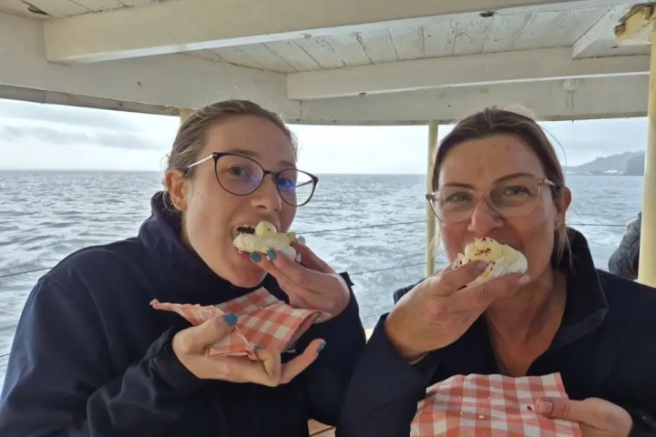 Two people on a boat eating food, holding checkered napkins.