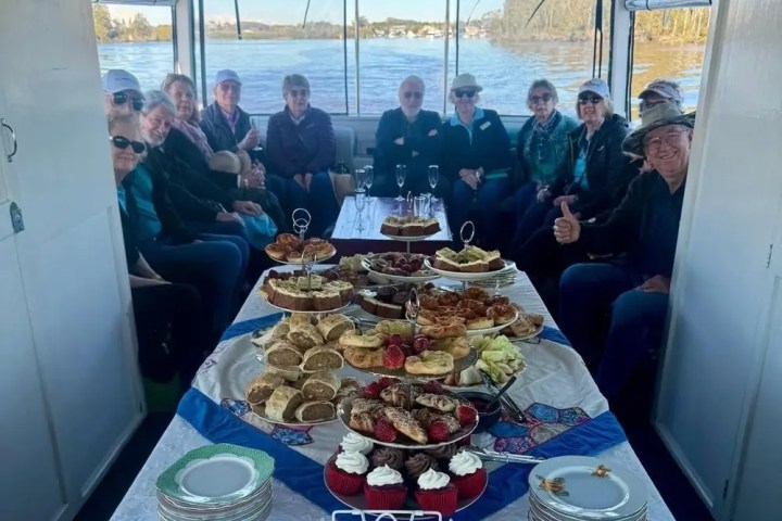 Group on a boat with a table of pastries and snacks, surrounded by water scenery.