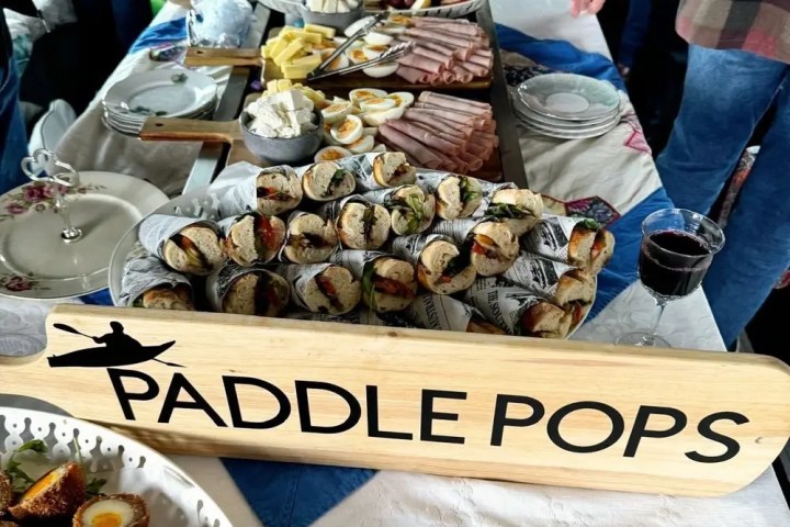 Buffet table with various dishes, a paddle labeled 'Paddle Pops,' and people in the background.