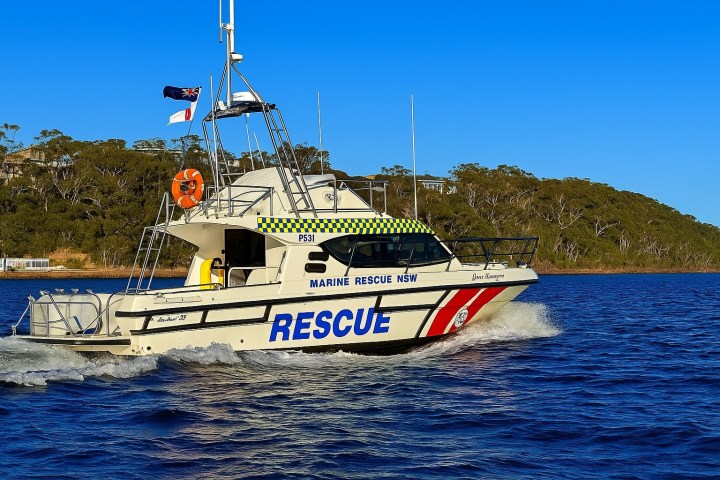 Marine rescue boat on water with trees and blue sky in the background.