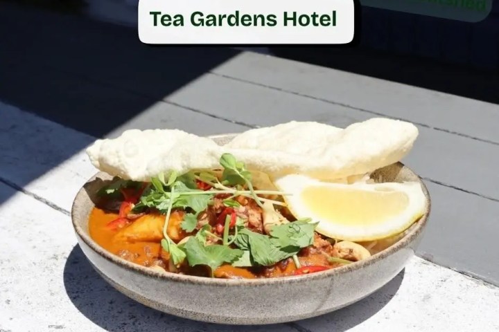 Bowl of curry with herbs, lemon, and wafers on a table, labeled 'Tea Gardens Hotel.'